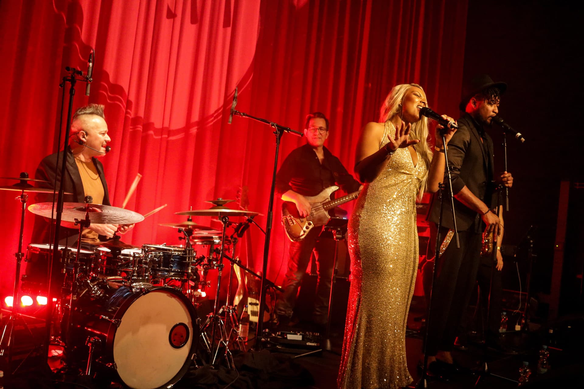 Die komplette Band auf der roten Vorhang-Bühne — professionelles Ensemble