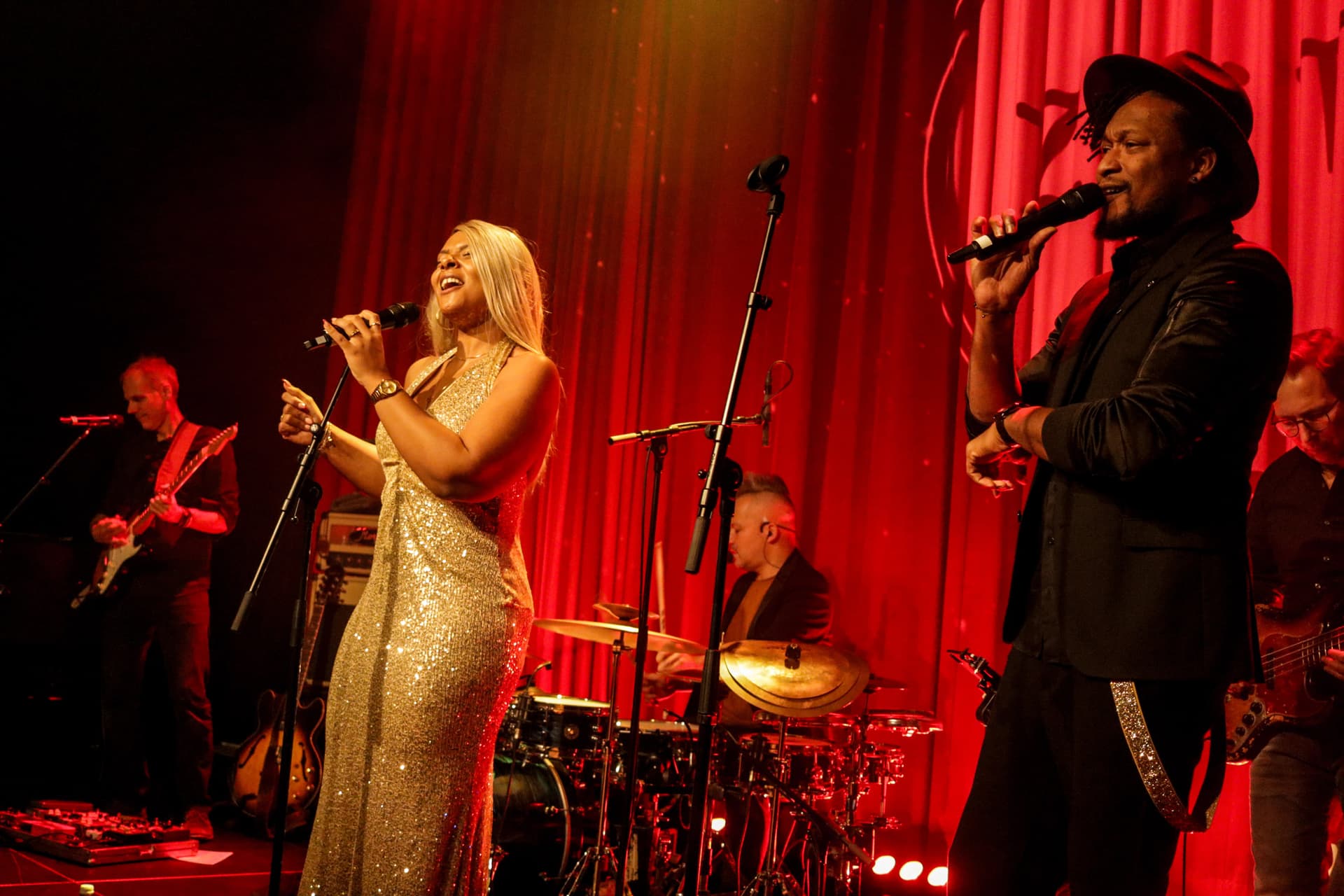 Amy Sue im Goldkleid und Klyive auf der roten Bühne, volle Band sichtbar