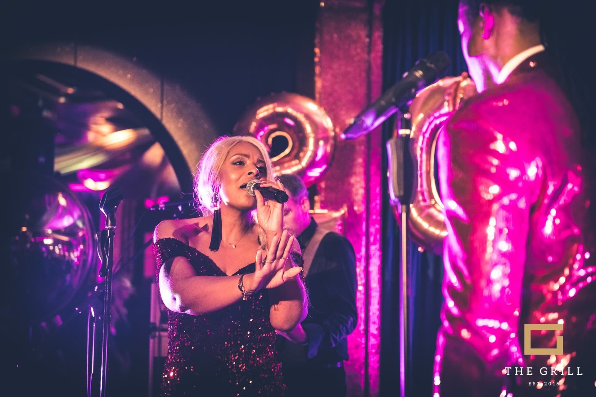 Amy Sue singend mit Saxophonist bei pinkem Bühnenlicht