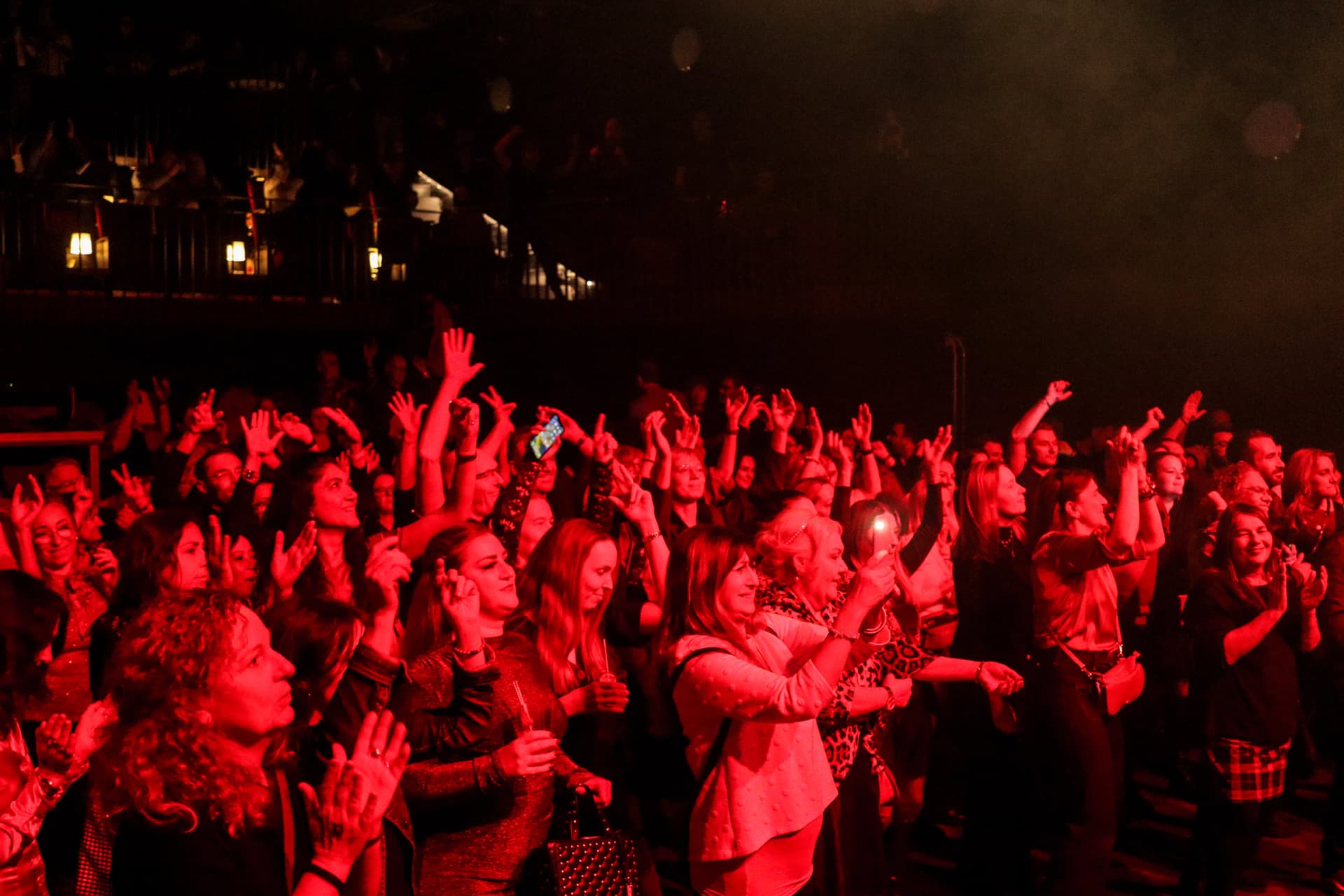 Jubelndes Publikum mit erhobenen Händen und Handys bei rotem Bühnenlicht
