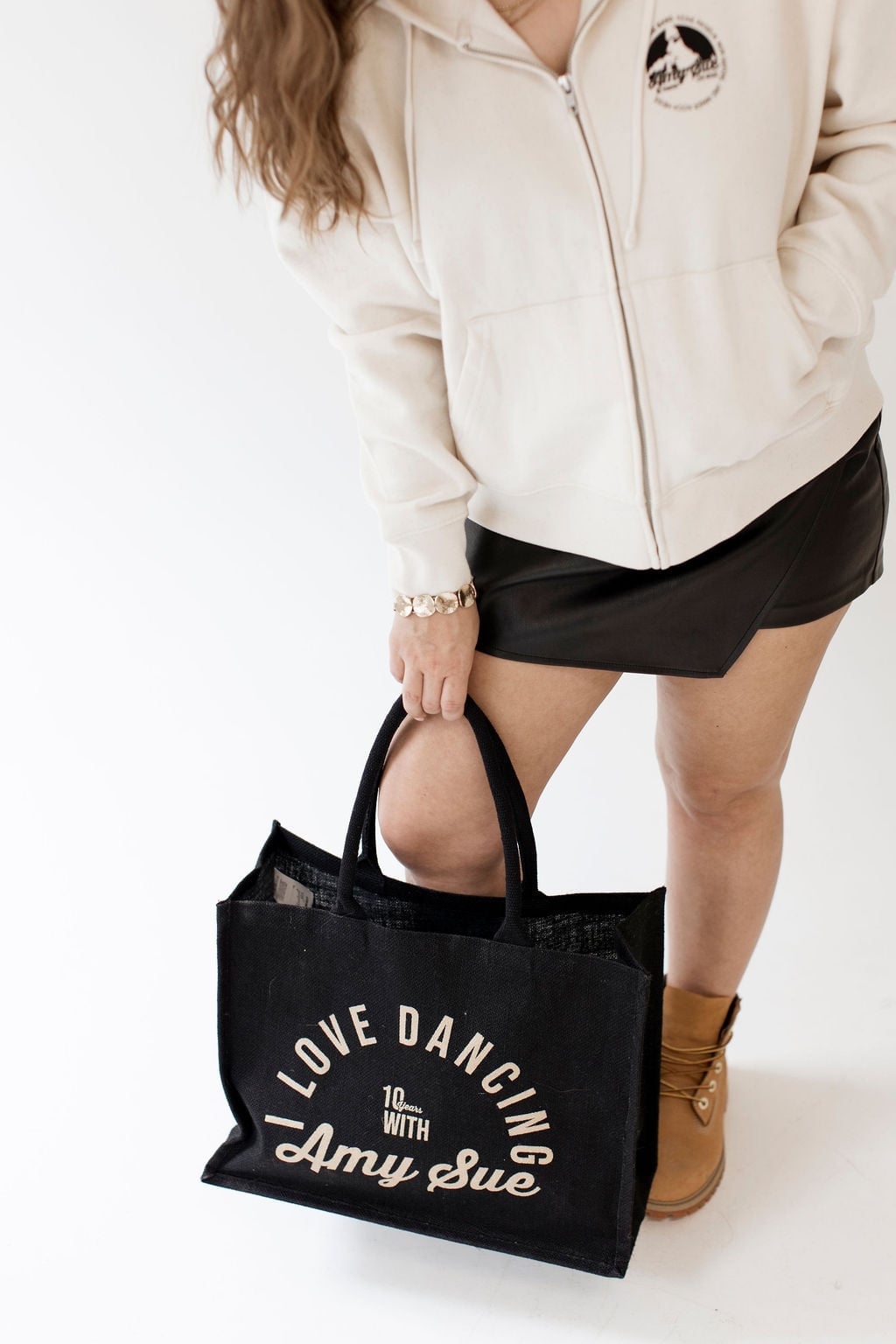Close-up der schwarzen Beachbag in Amy Sues Hand — Gold-Logo und „I love dancing with Amy Sue"-Schriftzug voll im Fokus