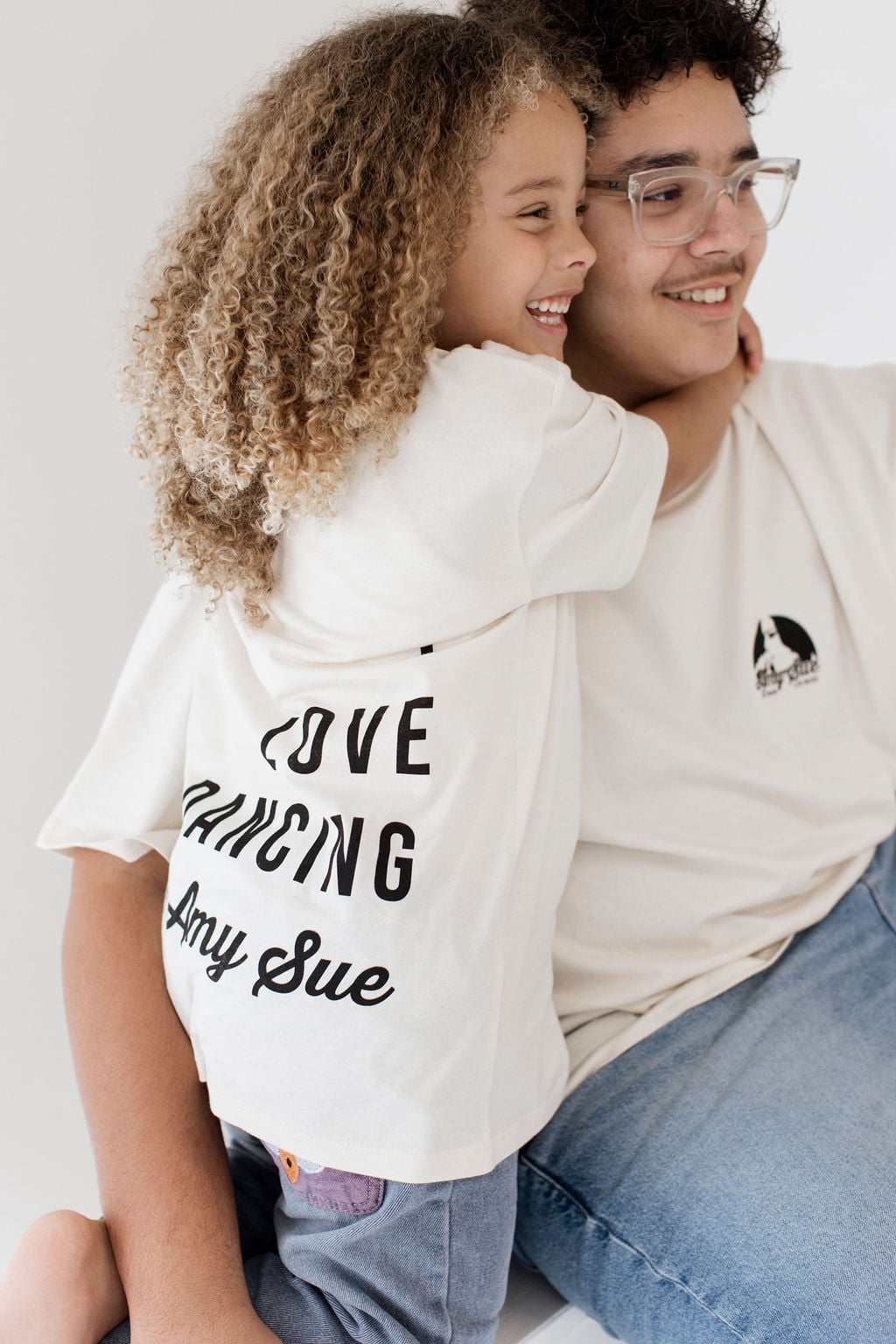 Kleines Kind umarmt einen Jugendlichen von hinten, „Love Dancing with Amy Sue"-Backprint des Kindershirts sichtbar